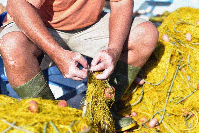 Greek fisherman repairing fishing net at the port Livadi, Serifo
