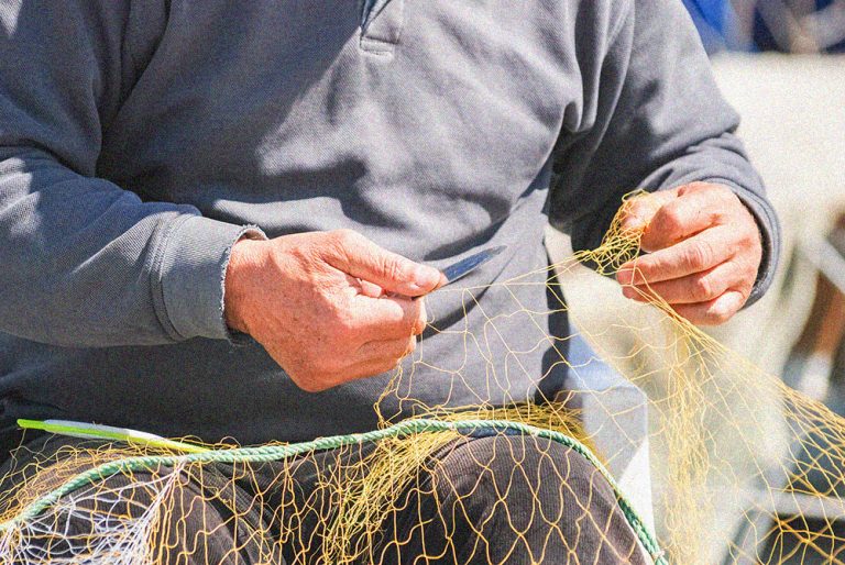 Fisherman hands repairing net with knife. Close up.